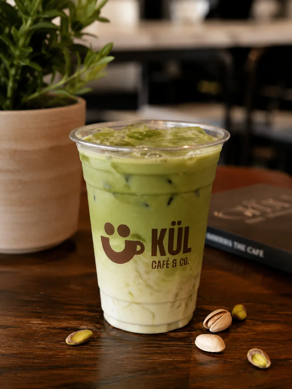 Iced Kül matcha latte in a branded cup on a café table.